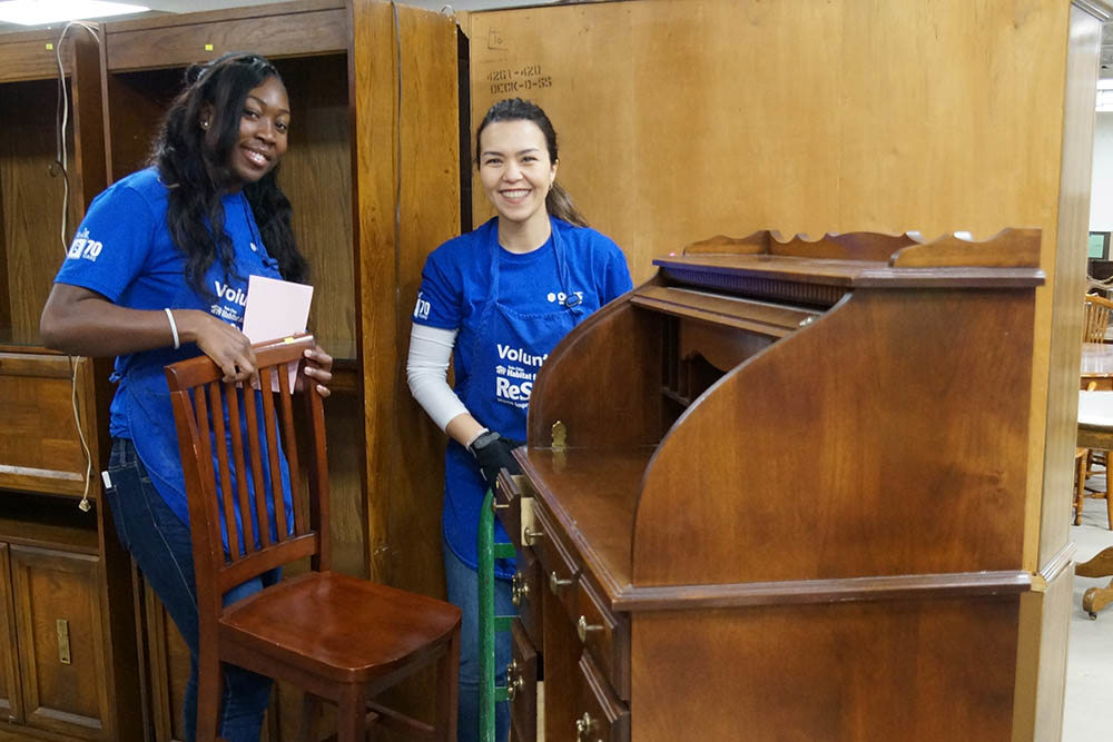 two women wearing blue shirts standing with furniture