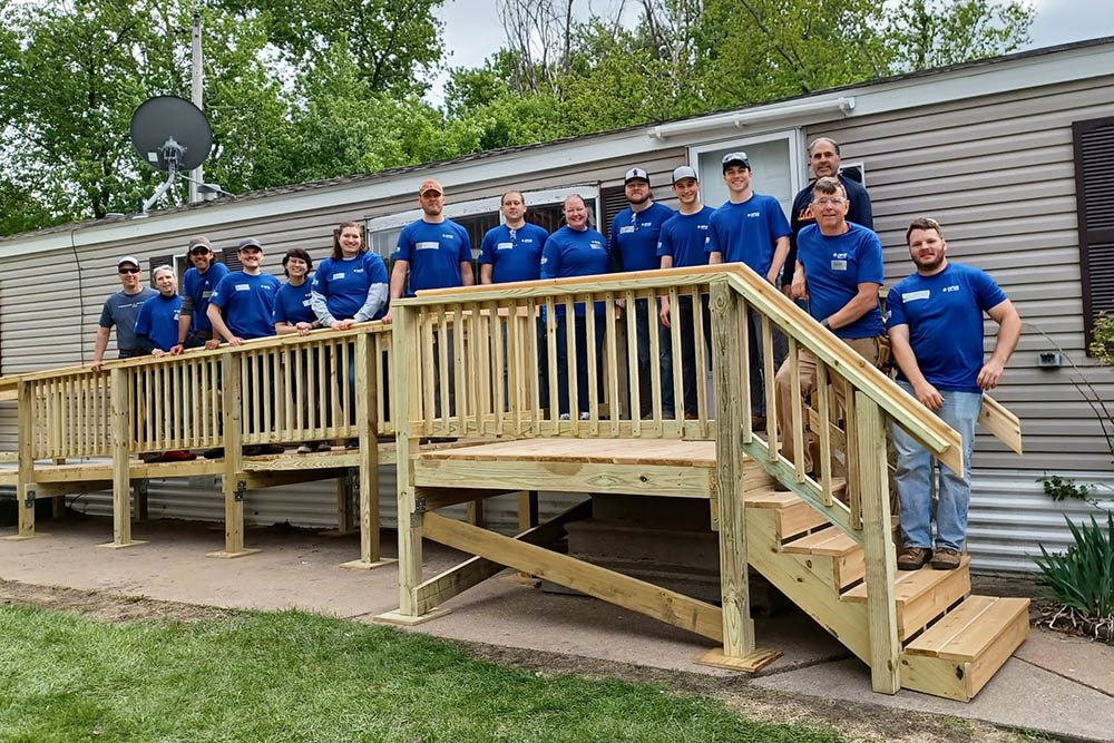 group of men and women wearing blue shirts standing on newly constructed ramp and front porch of house