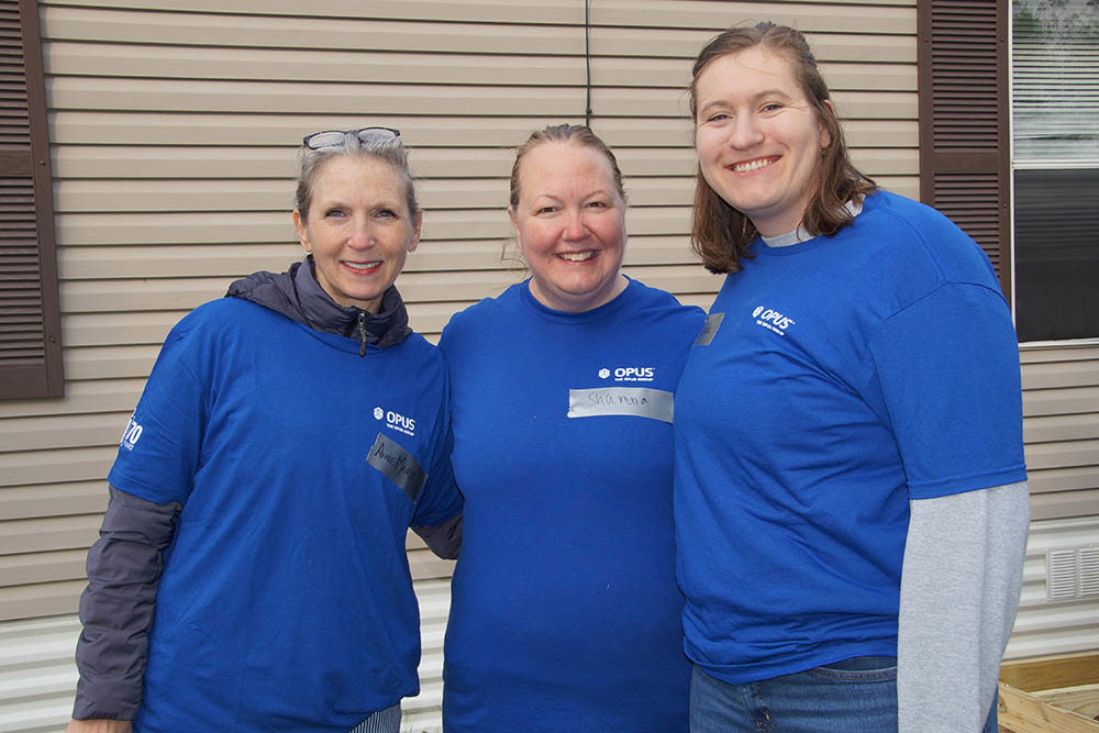 three women wearing blue shirts standing in front of a house