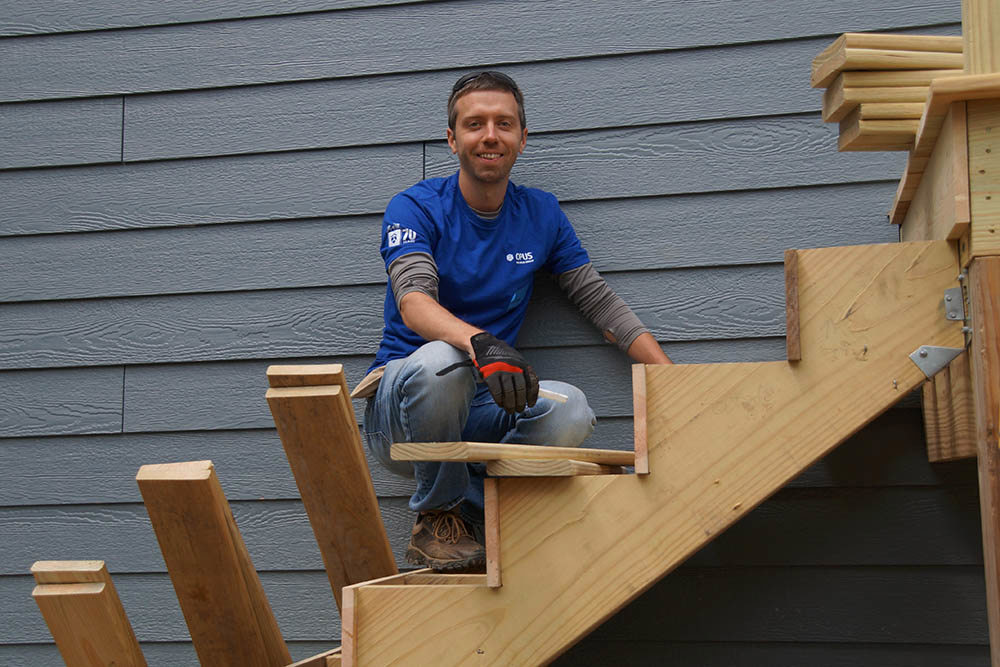 man smiling on stairs of porch under construction