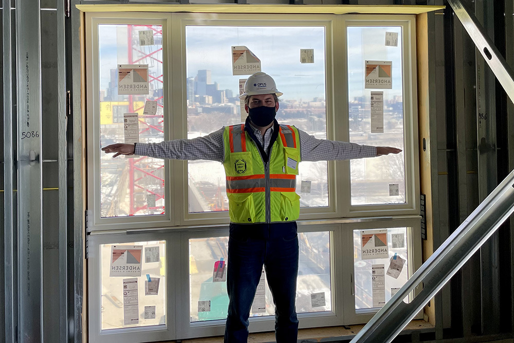 man wearing safety vest and hard hat in front of window with arms out to sides showing size of window