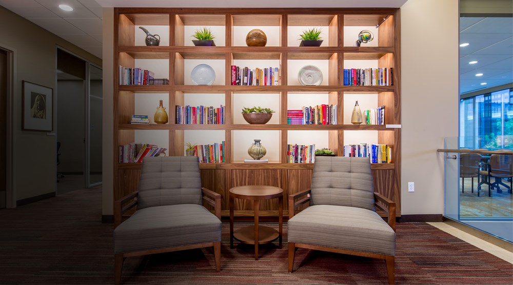 bookcase filled with plants, books and decorative items  with two chairs seperated by an end table in front