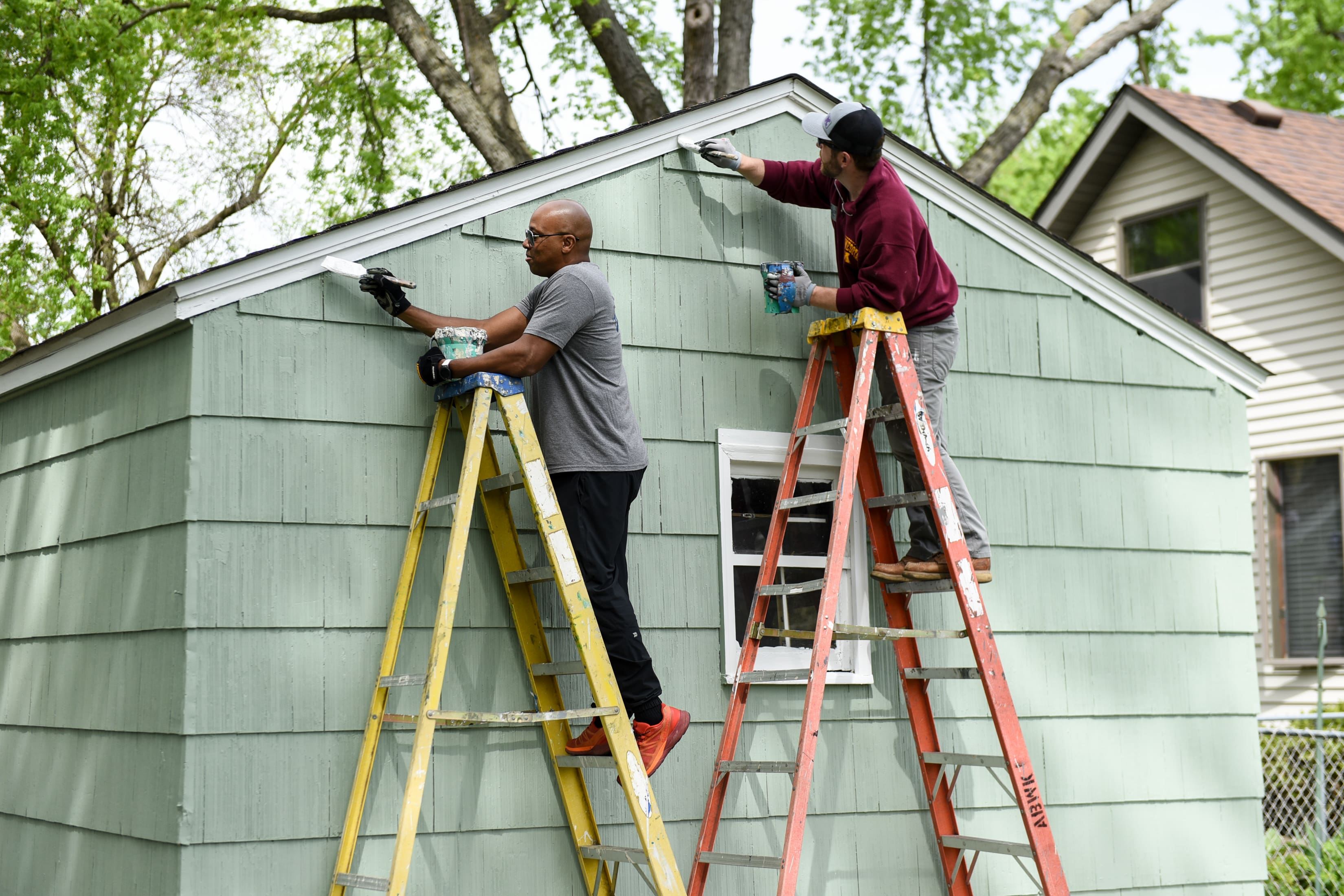 Two men on ladders paint the exterior of a home.