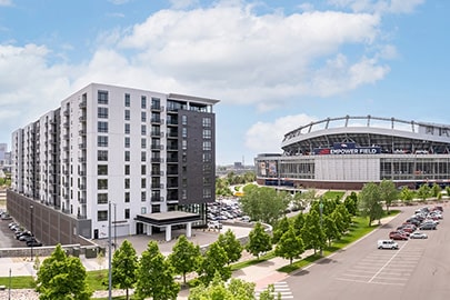 A multi-story apartment building with a line of healthy trees in front and near Empower Field where the Denver Broncos play.