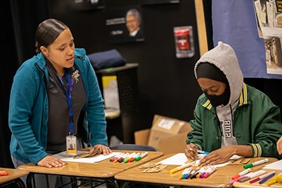 A woman stands near a student working at a table.