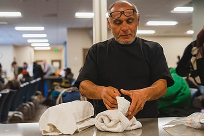 An older man with glasses push up on his forehead folds towels on a table.