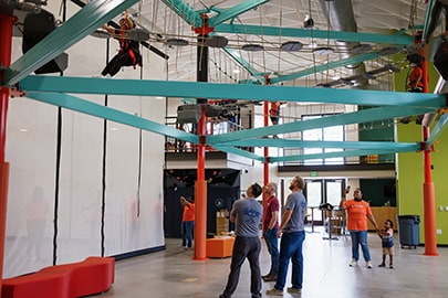 Several men stand below an indoor climbing structure.