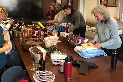 A group of people fill baskets around a long conference table filled with items.