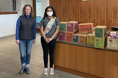 a woman and a girl stand in an office lobby with boxes of Girl Scout cookies