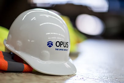 a hard hat with The Opus Group on the front sits on top of a high visibility construction vest