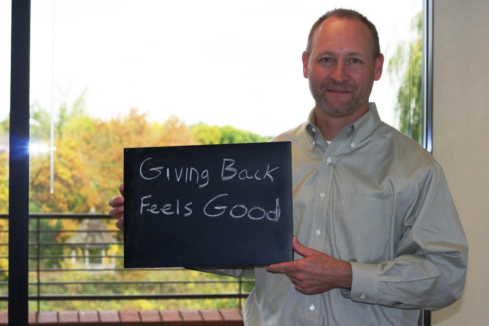 Man holding chalkboard with the words "Giving Back Feels Good"