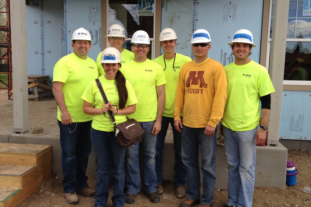 group of men and woman wearing hardhats standing in front of house under construction