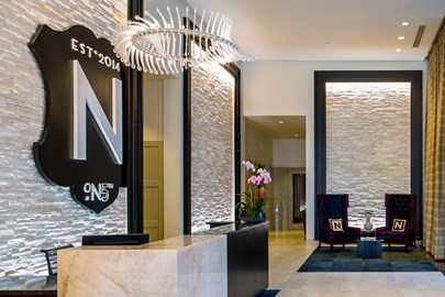 lobby of apartment building with large wall art that says, "N on 5th, Est. 2014" behind a marble reception desk on the left and a sitting area in the background on the right