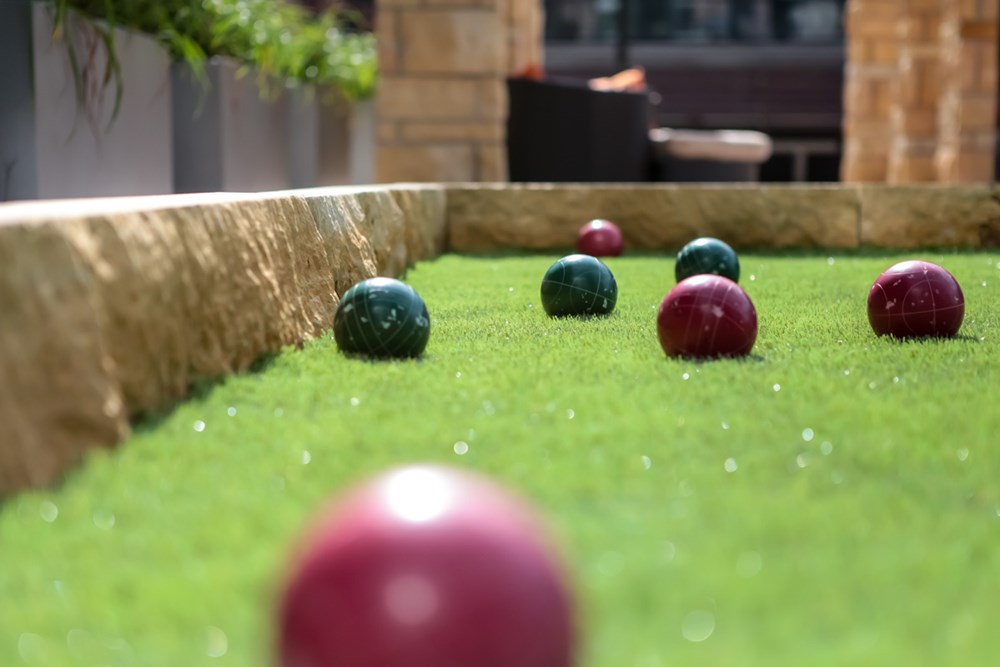 ground-level view of a bocce ball court with a red ball in the foreground and several balls in the background