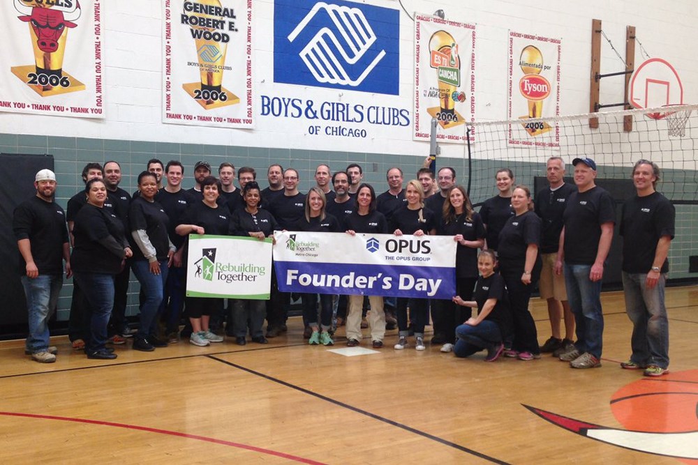 group of men and women in Boys & Girls Clubs of Chicago's gym holding banners saying, "Founder's Day" and The Opus Group and Rebuilding Together logos