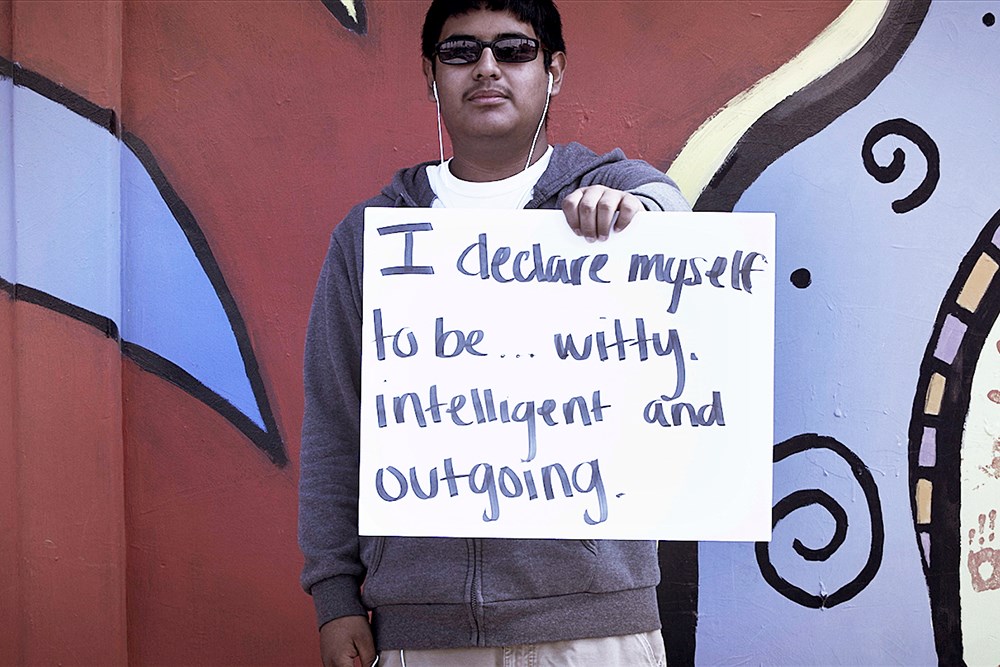 man wearing headphones and sunglasses holding a sign that says, "I declare myself to be...witty, intelligent and outgoing."