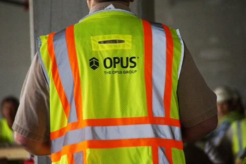 construction worker onsite wearing a high-visibility safety vest with The Opus Group logo