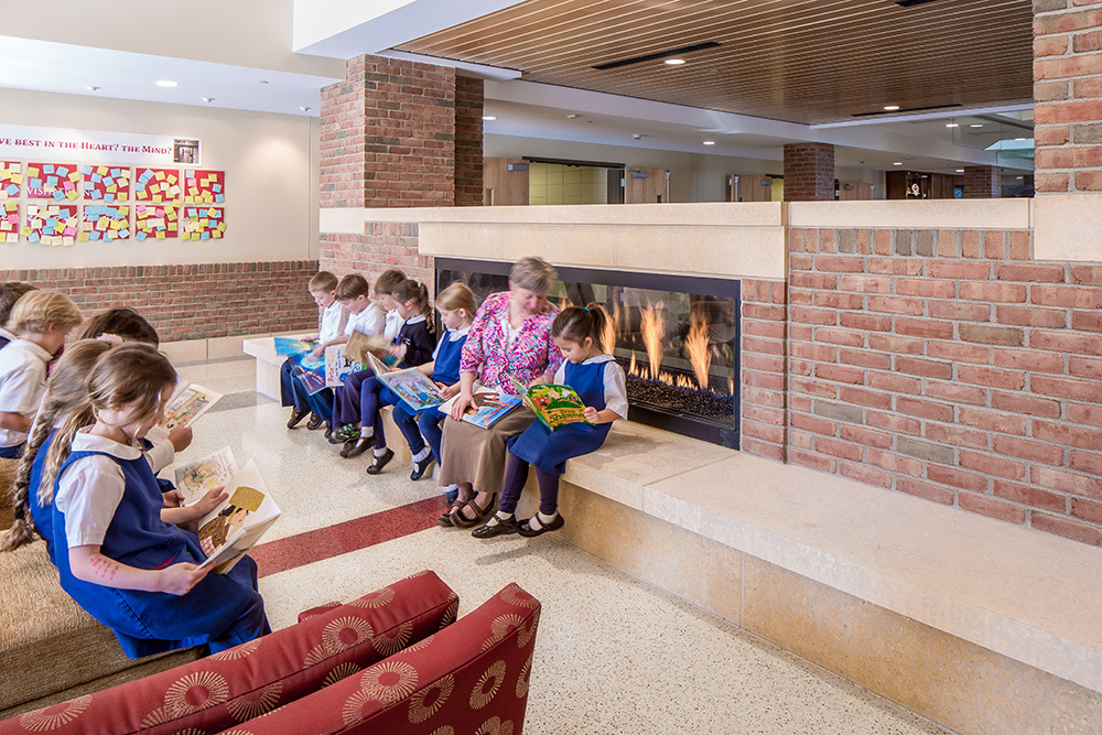 a teacher and young elementary students read in the Heart gathering area of Visitation School in Mendota Heights, Minnesota