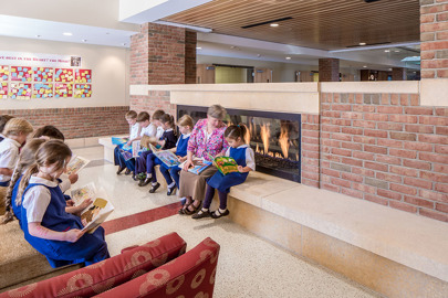 young private school children and their teacher read in front of a fireplace