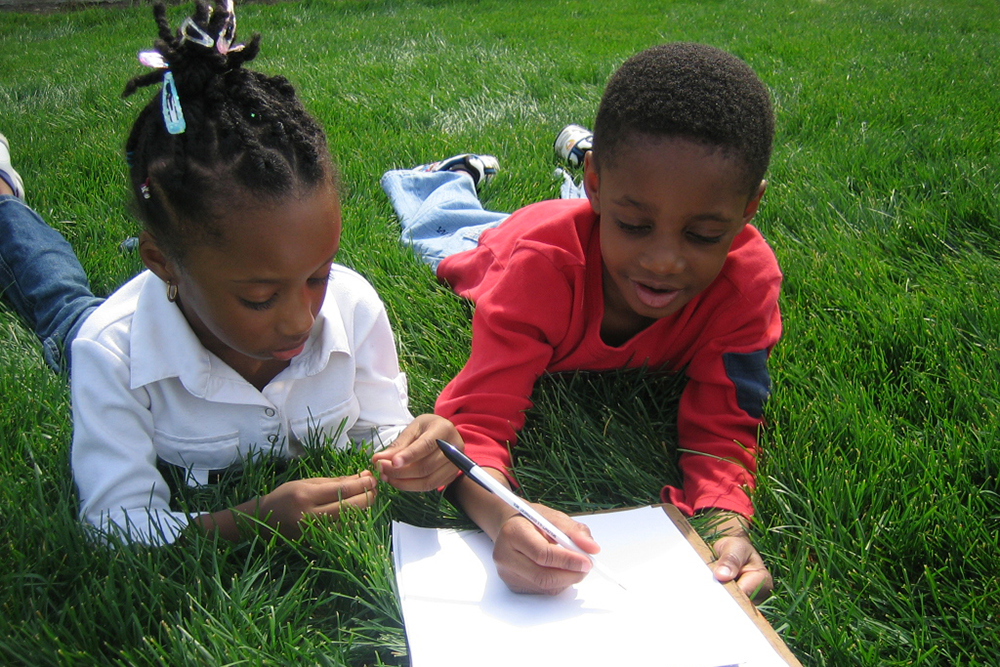 boy and girl laying on grass writing on paper