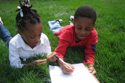 boy and girl laying on grass writing on paper