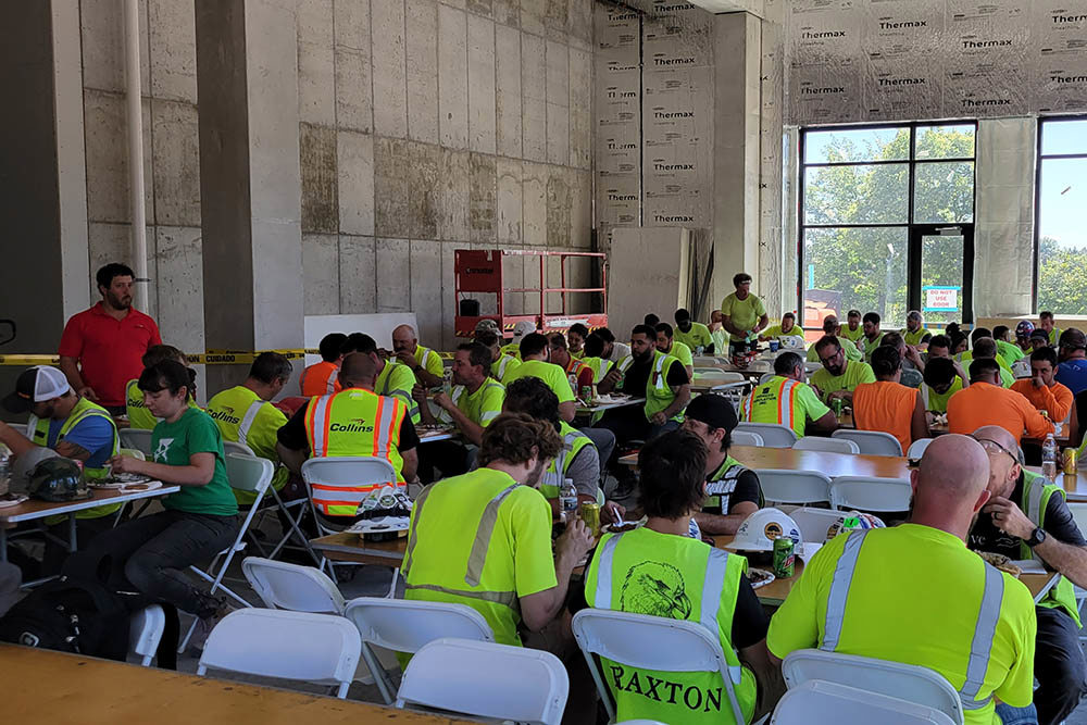 men and women in safety vests seated at tables inside an unfinished building