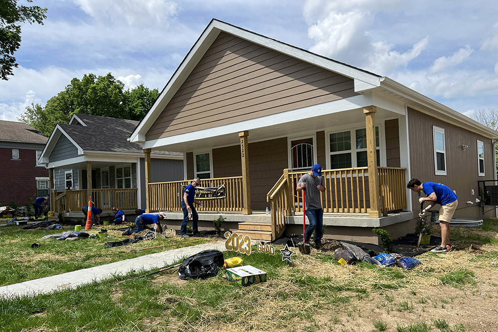 men and women wearing blue shirts working on landscaping in front of two newly built houses