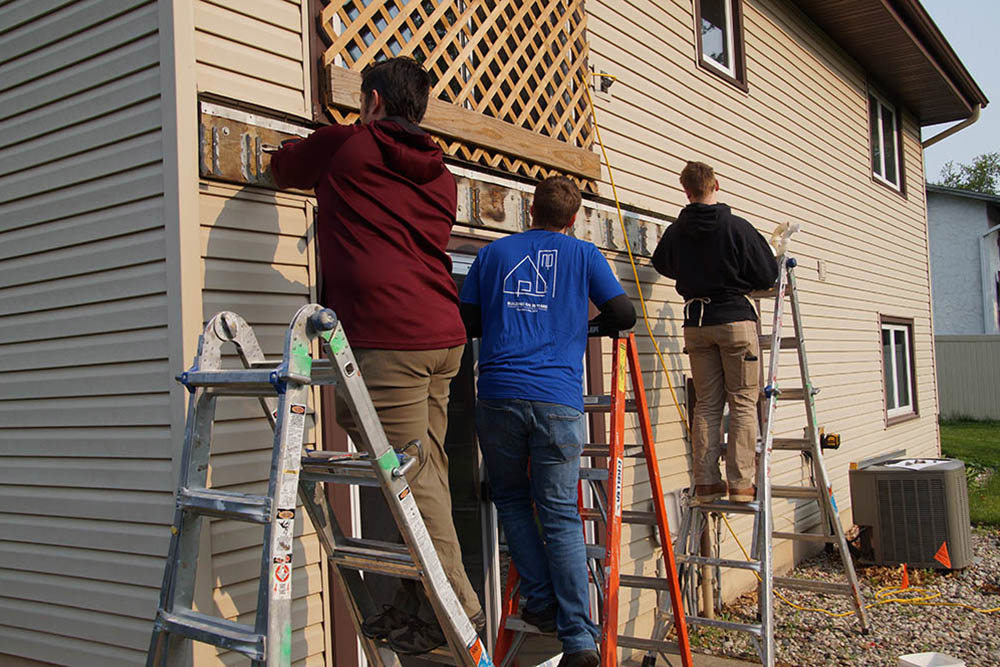 three men on ladders working on the siding of a house