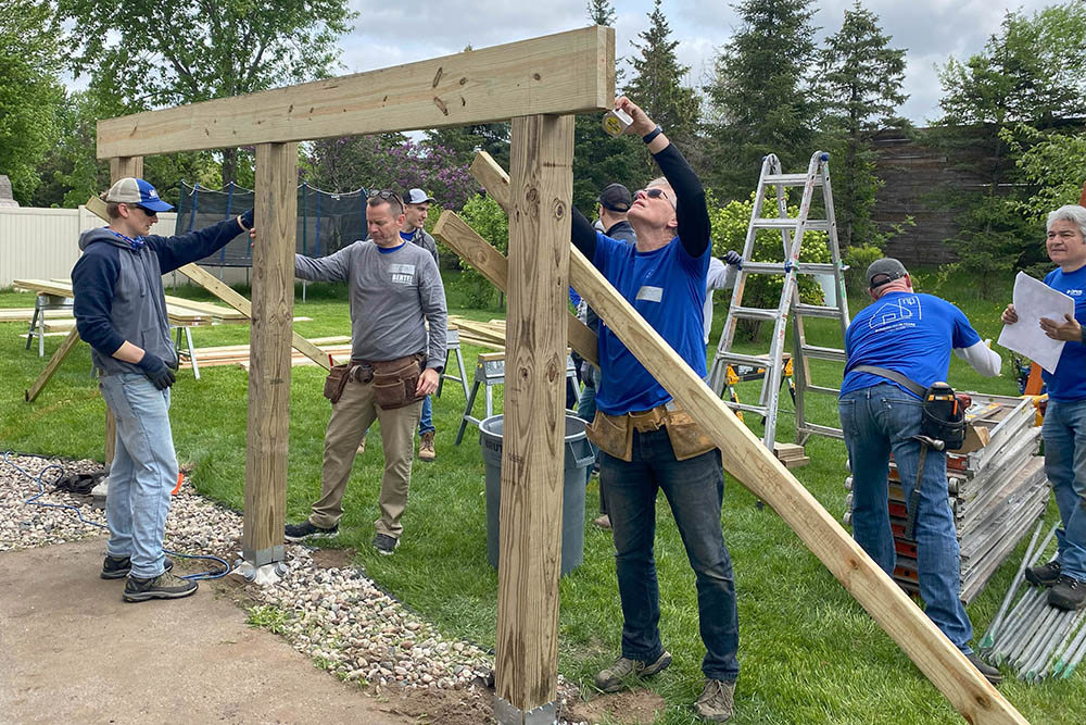 men outdoors building a wood frame in the foreground and men organizing with construction materials in the background