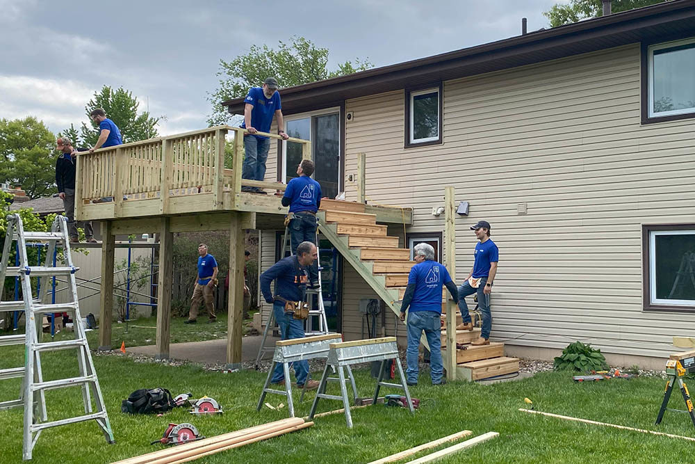 men building a second-floor deck and staircase on the back of a house