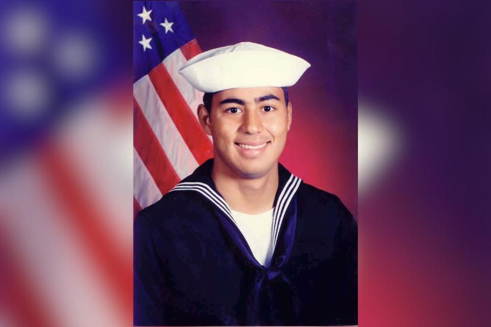 man in U.S. Navy uniform with U.S. flag in background