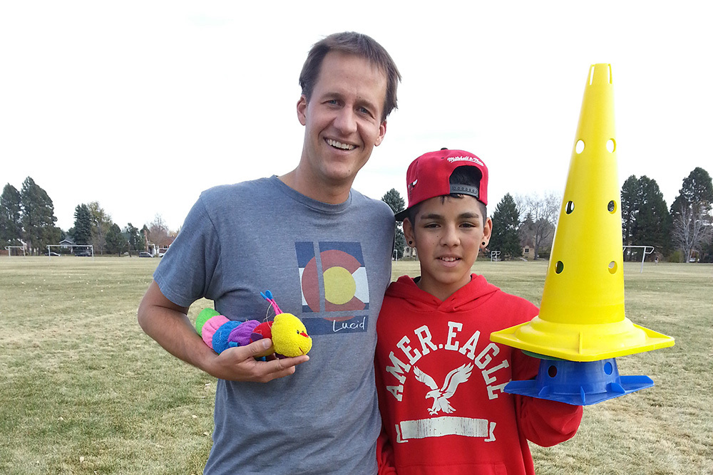 man holding a stuffed caterpillar and boy holding stacked plastic cones on athletic field