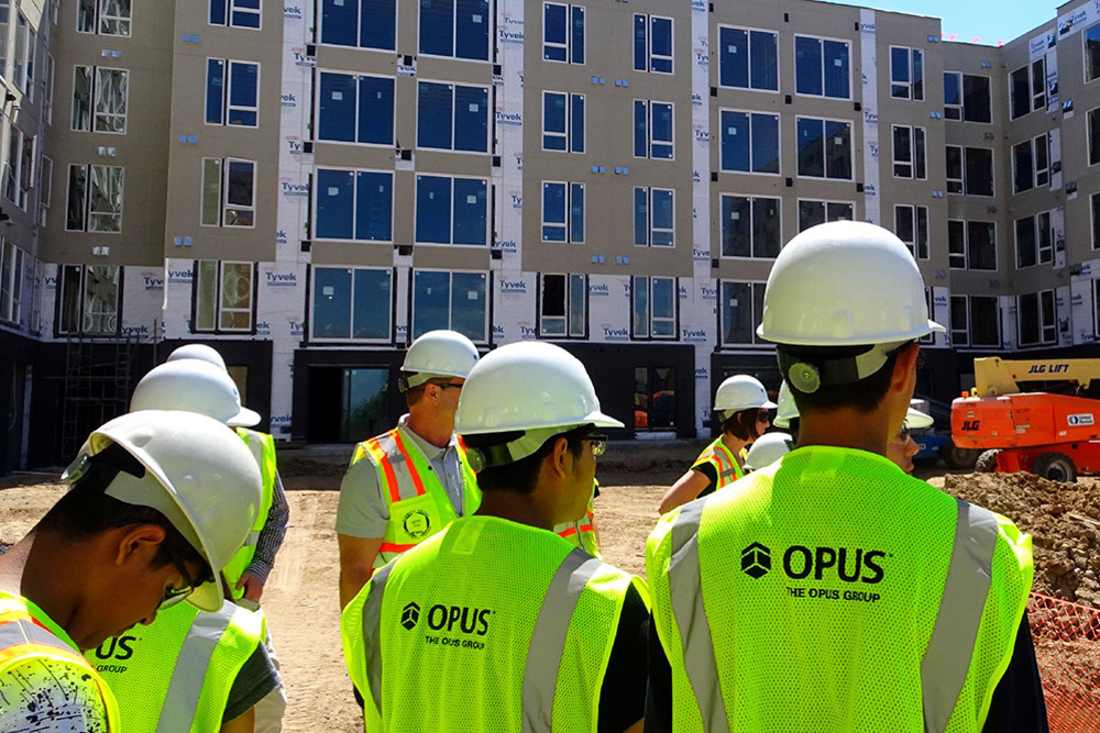 group of teenagers in safety vests and helmets with an apartment building under construction in background