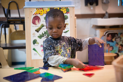 young boy standing at a table while playing with colorful blocks