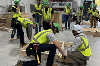 a group of male teenagers wearing safety vests and hardhats inside a warehouse learning how to build wooden frames for walls