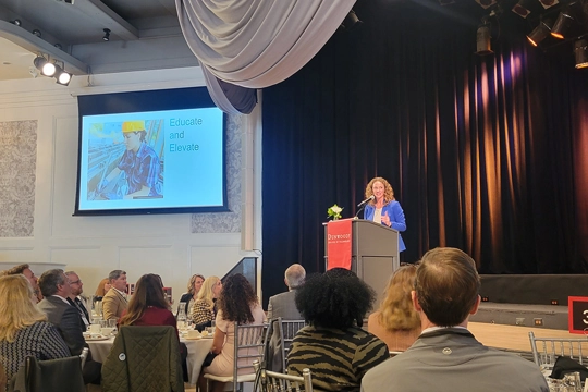 woman at podium on stage speaking to audience