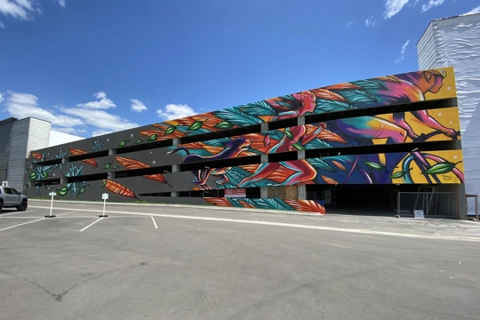 colorful mural of a bicyclist, runner, dog and leaves on the side of an apartment buildings' parking garage