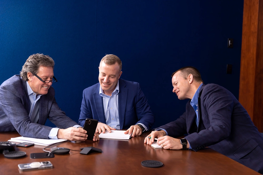 three men in professional attire sitting around a table in a conference room