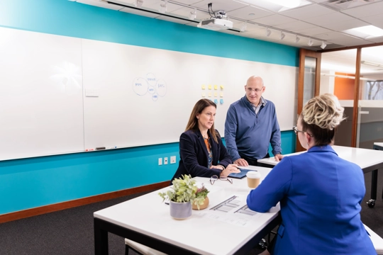 two women and a man seated around a table in a conference room