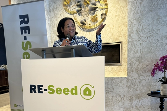 person behind a podium with sign reading "RE-Seed"