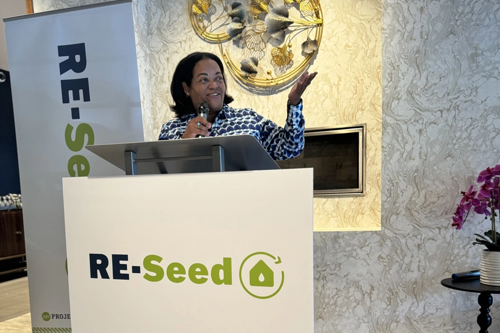 person behind a podium with sign reading "RE-Seed"
