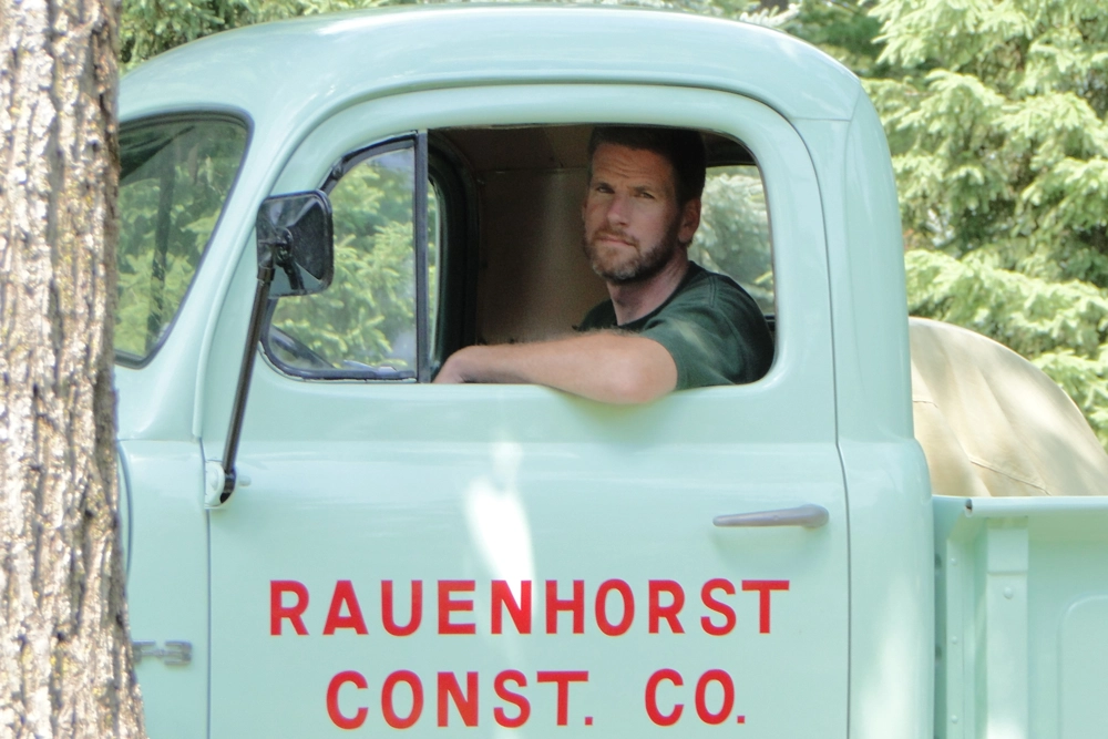 antique pickup truck with man looking out door window, and sign on door reads "Rauenhorst Const. Co."