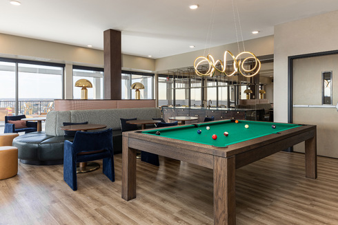 a clubroom space in an apartment building with a billard table in the foreground and tables and chairs and kitchen in the background