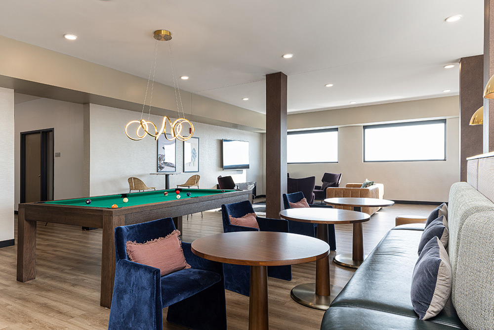 a clubroom space in an apartment building with tables with chairs and booth seating on the right and a billard table on the left and a seating area in the background
