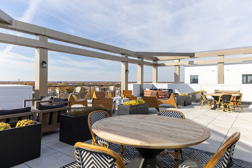 a rooftop outdoor living area in an apartment building with a round table and four chairs in the foreground and seating areas and a table and chairs in the background