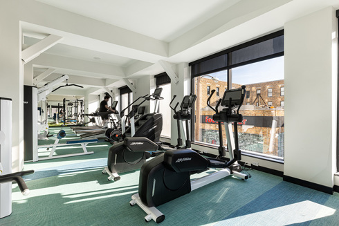 fitness center in an apartment building with a row of exercise equipement along an exterior wall with windows