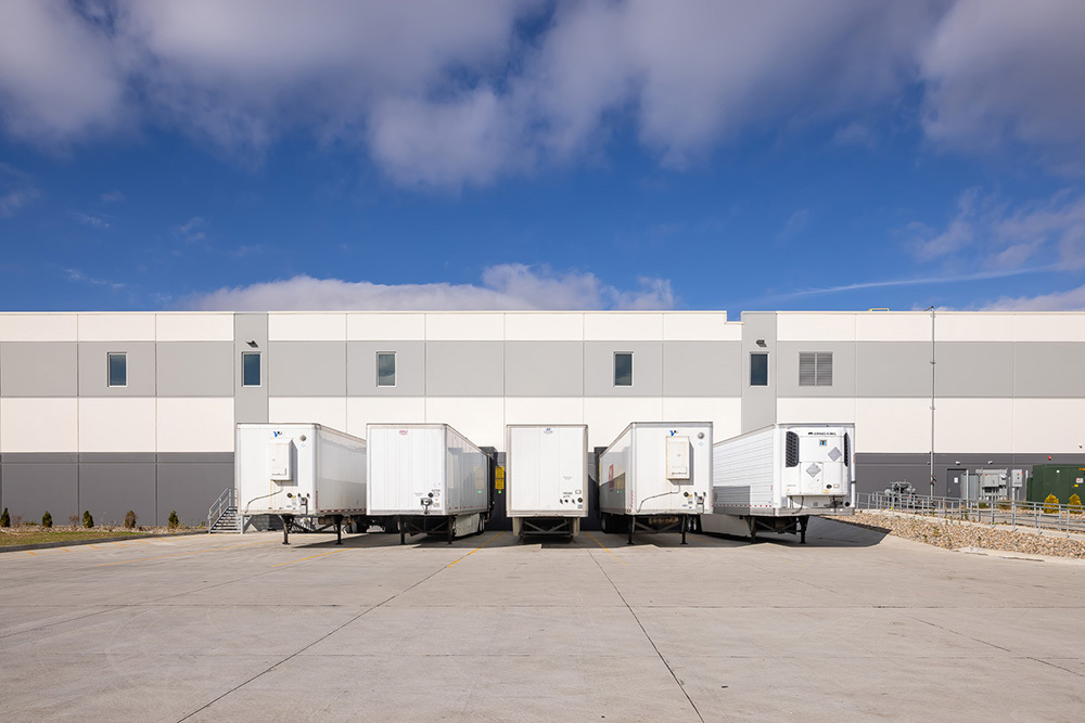 five truck trailers parked in front of an industrial building's dock doors