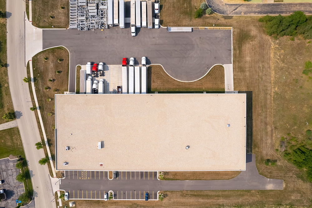aerial view of industrial building, directly over building with trucks at dock doors on top half and front parking lot on bottom half of image