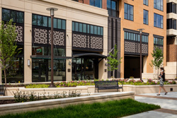 street view of a mixed-use development with raised flower beds, park bench and sidewalk in the foreground and retail space in the background
