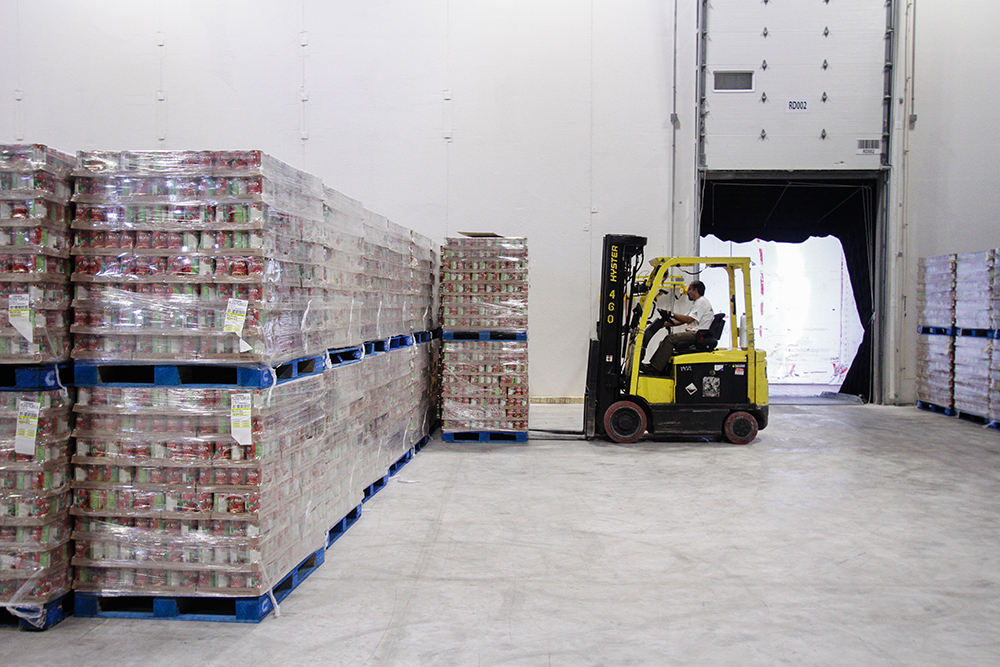 warehouse in an industrial building with wrapped pallets stacked on the left and a forklift in front of an open dock door on the left in the background